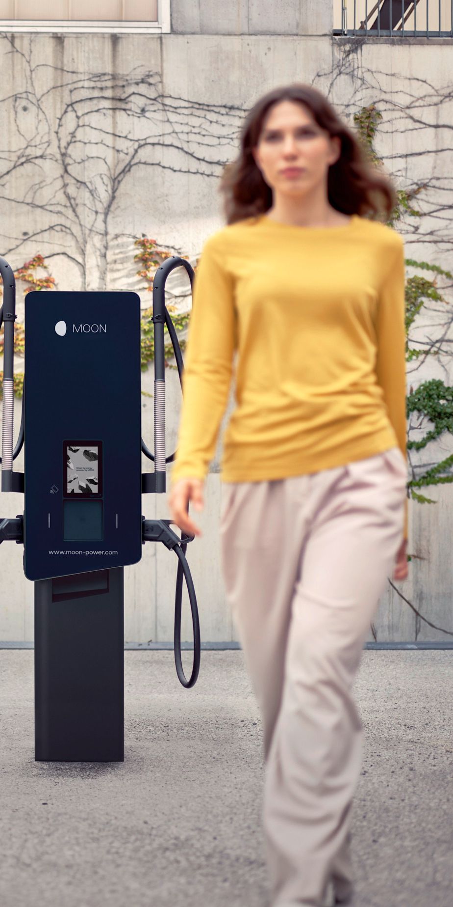 Žena prochází před nabíjecí stanicí s autem v pozadí