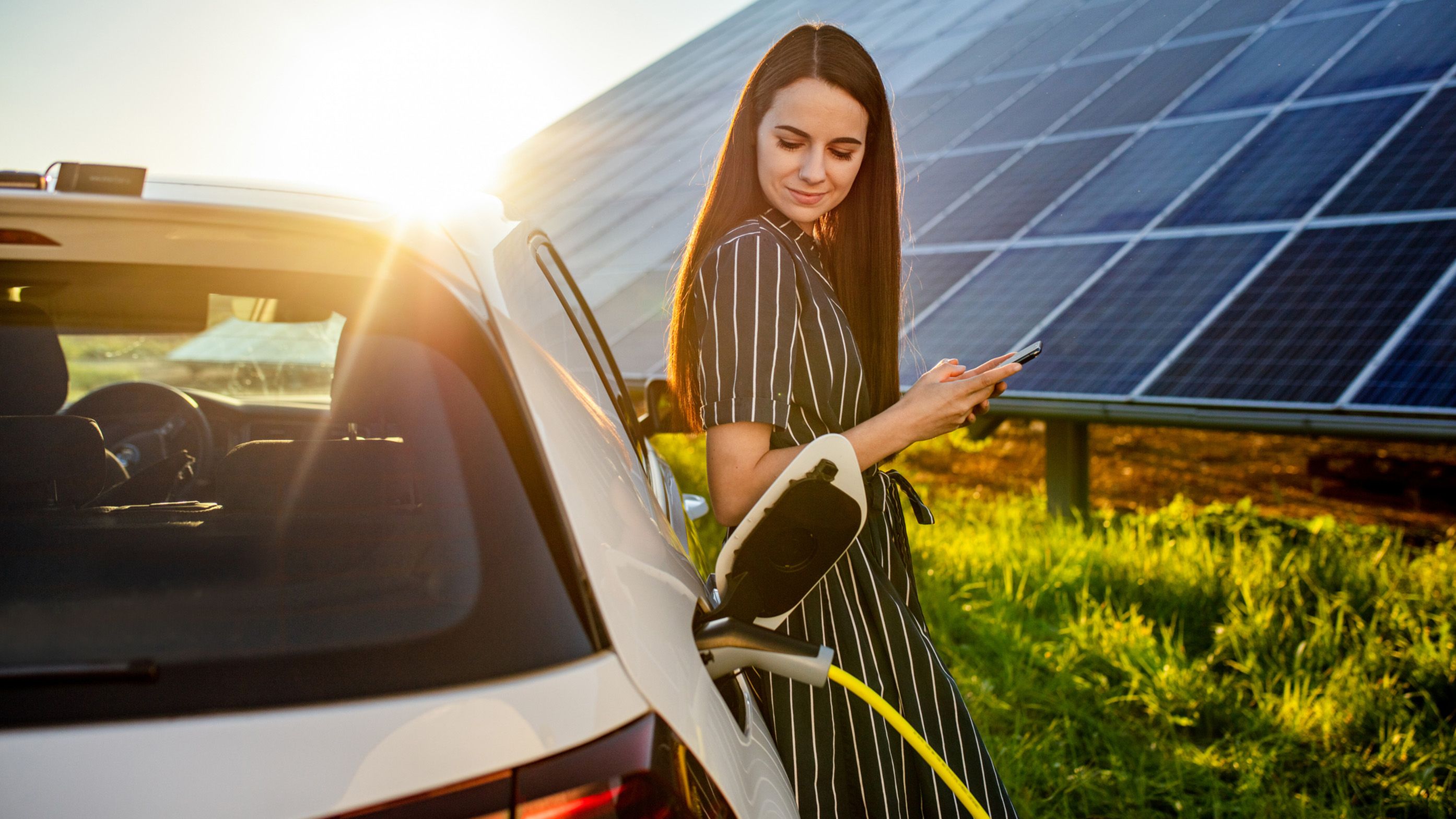 Žena opřená o nabíjející se auto před fotovoltaickým systémem