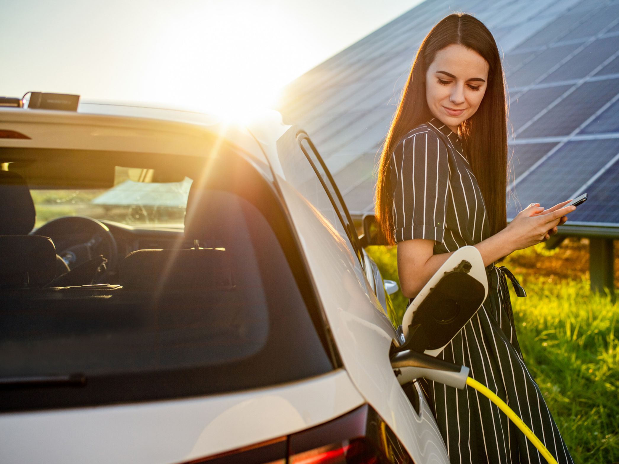 Žena opřená o nabíjející se auto před fotovoltaickým systémem