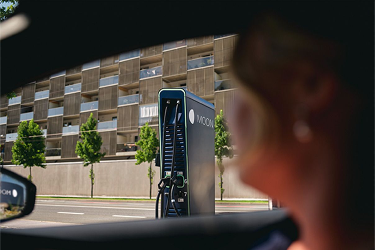 Osoba sedící v autě s nabíjecí stanicí v pozadí