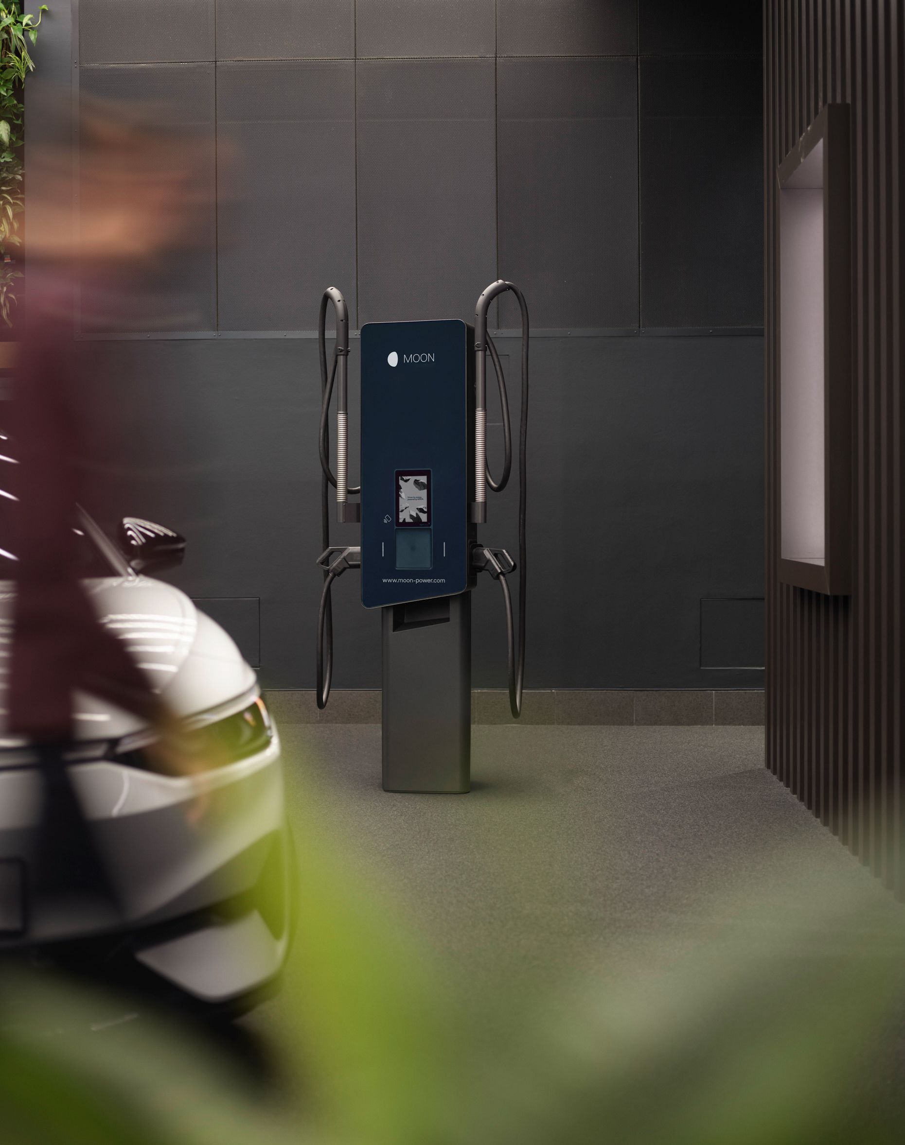 Nabíjecí stanice před šedou zdí s autem v popředí