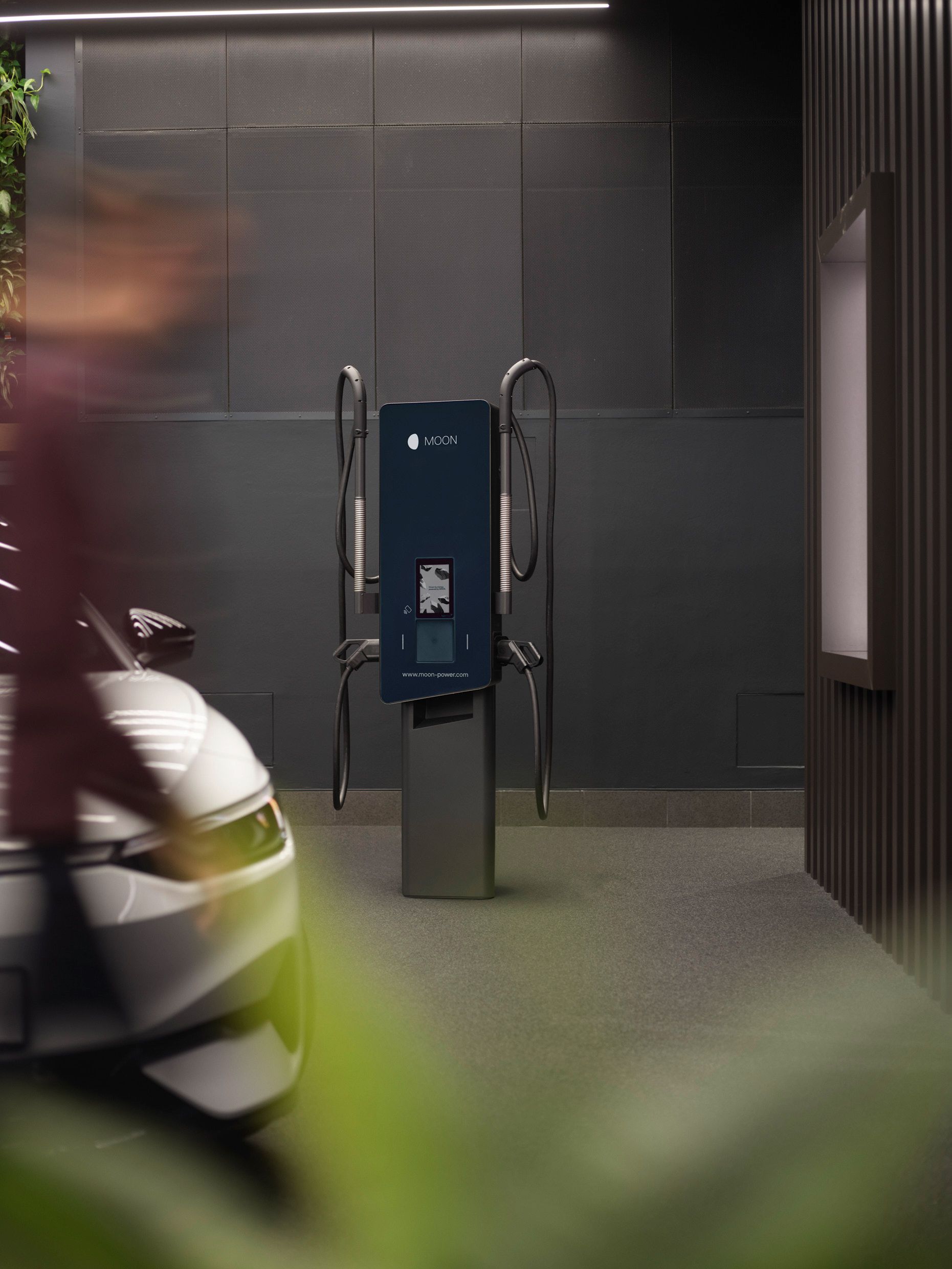 Nabíjecí stanice v místnosti s šedými stěnami a autem v popředí